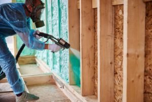 A male insulation technician professionally applying spray foam insulation to the walls of a home 