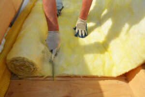 Insulation installer cutting and applying batt insulation to a home